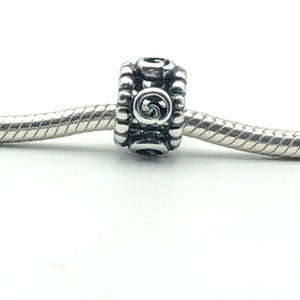 May include: A silver-toned charm bead with a spiral design in the center. The bead is cylindrical with a textured, beaded pattern around the edges. It is strung on a silver chain, set against a white background.
