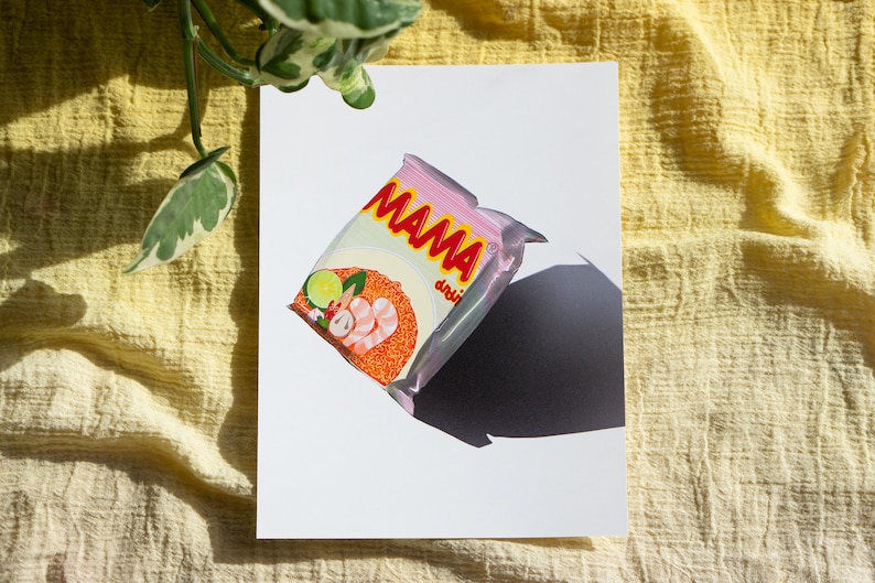 May include: A pink and red instant noodle packet with the word "MAMA" printed on it. The packet shows a bowl of noodles with prawns, lime, and other ingredients.