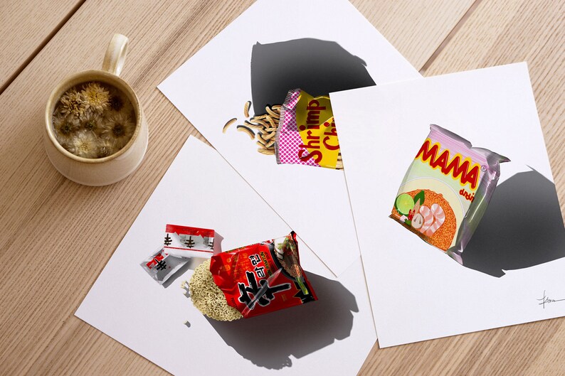 May include: Three different instant noodle packets on white paper. The packets are all different brands and flavours. One packet is red with white text, another is yellow with pink and white text, and the last is pink with white text. The packets are all slightly open and the noodles are spilling out.