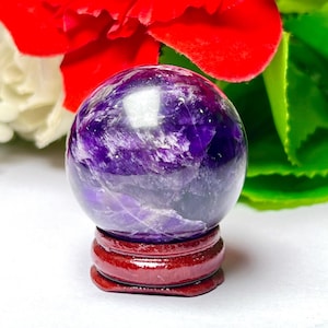 May include: A purple amethyst crystal ball on a wooden stand. The ball is smooth and polished, with a swirling pattern of purple and white.