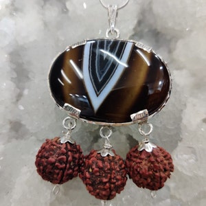May include: A silver pendant with a brown and white agate stone and three red beads hanging from it.