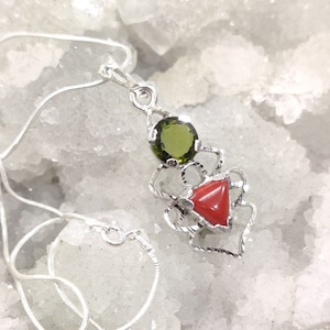 May include: A silver chain necklace with a pendant featuring a green gemstone and a red coral stone set in a silver filigree design.