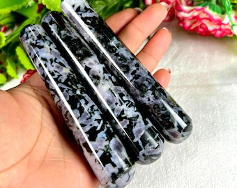 May include: Three polished, cylindrical stones with a mottled pattern of black, white, and lavender. The stones are smooth and rounded, with a glossy finish. The stones are held in a hand.