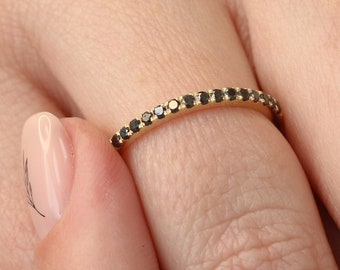 May include: A thin gold band ring with a row of small black diamonds.
