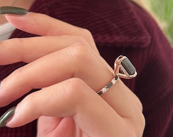 May include: A rose gold ring with a black gemstone and small clear gemstones on the band.