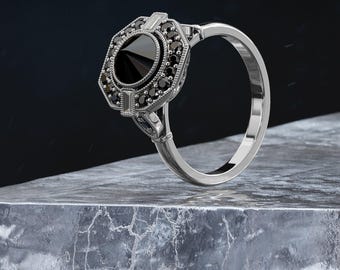 May include: A silver ring with a black octagon-shaped gemstone surrounded by smaller black gemstones. The ring has a delicate, intricate design.
