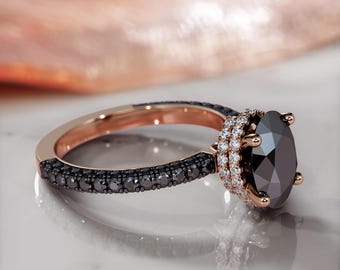 May include: A rose gold engagement ring with a black diamond center stone surrounded by a double halo of smaller white diamonds. The band is set with black diamonds.