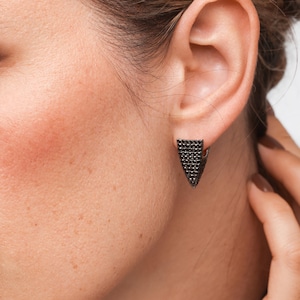 May include: A pair of black triangle-shaped earrings with a pave setting of black stones.