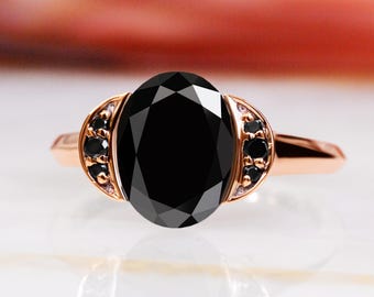 May include: A rose gold engagement ring with a large oval black diamond and smaller black diamonds set in the band.