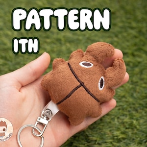 May include: A brown plush keychain shaped like a beetle with a white face and black eyes. The keychain is attached to a silver key ring. The text "PATTERN ITH" is visible in the image.