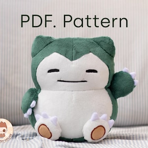Puede incluir: Juguete de peluche verde y blanco que se asemeja a un personaje de Pokemon. El juguete tiene un cuerpo redondo con una gran barriga blanca y pequeñas orejas verdes. El juguete tiene una expresión amigable con los ojos cerrados y una pequeña boca negra.