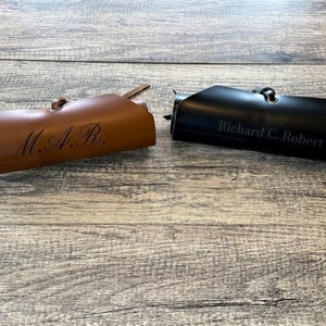 May include: Two rolled-up leather cases with personalized engravings. The brown case reads "M.A.R." and the black case reads "Richard C. Robert".