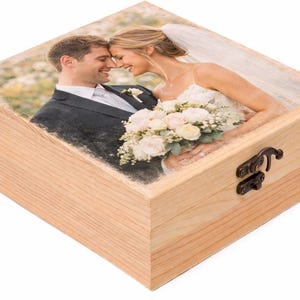 Puede incluir: Caja de recuerdos de madera clara con una imagen impresa de una pareja sonriente en la tapa. La caja tiene un cierre metálico. La imagen de la tapa muestra a una novia y un novio abrazándose, con la novia sosteniendo un ramo.