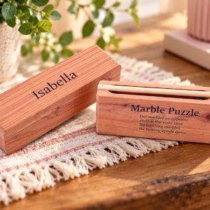 May include: A rectangular wooden box with the name Isabella engraved on the top and a second wooden box labeled Marble Puzzle with instructions to get marbles on opposite ends at the same time, no touching marbles, and no turning upside down.
