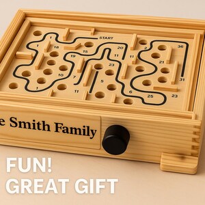 Puede incluir: Un juego de laberinto de madera con un dise&ntilde;o de laberinto negro y caminos numerados. El juego tiene una perilla negra y el texto "The Smith Family" es visible. Tambi&eacute;n se muestran las palabras "FUN! GREAT GIFT".