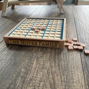 May include: A wooden game board with a blue border and the text "THE NOYES FAMILY" on the front. The board is divided into a grid of squares. There are small wooden tiles with numbers on them scattered around the board.