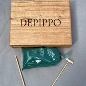 May include: A wooden box with the name "DEPIPPO" engraved on the lid. The box contains a bag of green sand, two wooden sticks, and a small wooden rake.