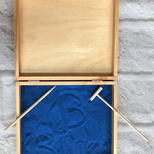May include: A wooden box with a blue sand tray and two wooden tools. The box is open and the sand tray is visible. The tools are a rake and a small shovel.