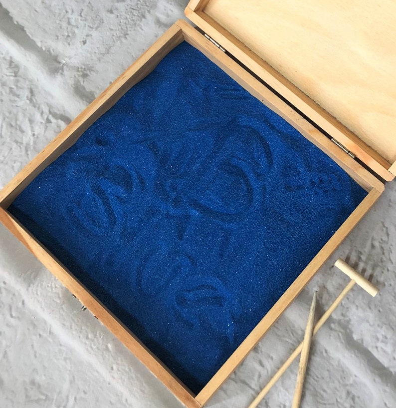 May include: A wooden box with a blue sand tray inside. The box is open and there is a small rake next to it.