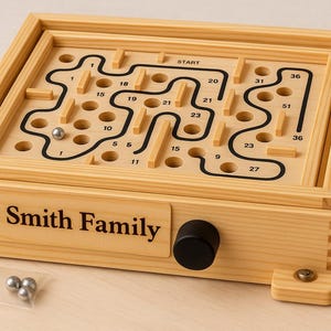 Puede incluir: Juego de laberinto de madera con un dise&ntilde;o de laberinto negro y caminos numerados. El juego presenta una perilla negra y el texto "The Smith Family". Incluye tres bolas de metal plateado.