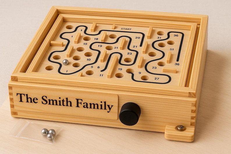 Puede incluir: Juego de laberinto de madera con un dise&ntilde;o de laberinto negro y caminos numerados. El juego presenta una perilla negra y el texto "The Smith Family". Incluye tres bolas de metal plateado.