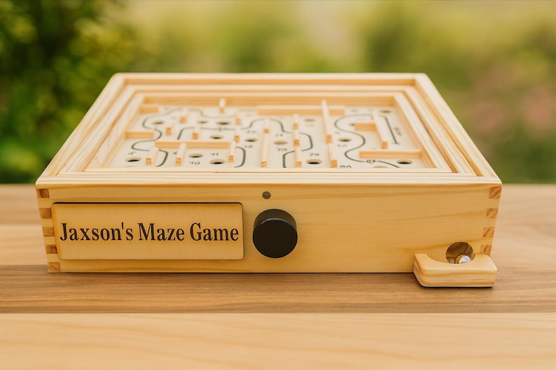 Puede incluir: Un juego de laberinto de madera con el texto "Jaxson's Maze Game" en la parte delantera. El juego presenta una perilla negra y una peque&ntilde;a bola de metal. El laberinto es una serie de caminos y agujeros.