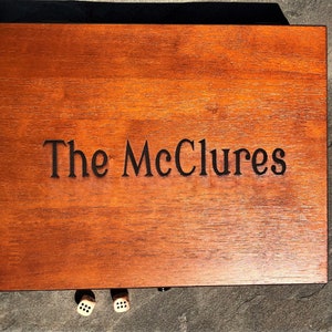 May include: A wooden box with the inscription "The McClures" on the top. Two dice are visible in front of the box.
