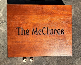 May include: A wooden box with the inscription "The McClures" on the top. Two dice are visible in front of the box.