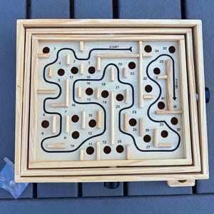 Puede incluir: Rompecabezas de laberinto de madera con un camino negro y agujeros numerados. La palabra "START" est&aacute; al principio del camino. El laberinto est&aacute; dentro de un marco de madera. Un rompecabezas divertido y atractivo para todas las edades.