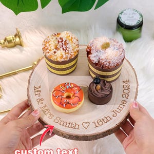 May include: A wooden round cake stand with a natural bark edge. The stand has a custom engraved message: "Mr. & Mrs. Smith ♥ 16th June 2024". The stand is decorated with a donut, a chocolate dessert, and two mini cakes.