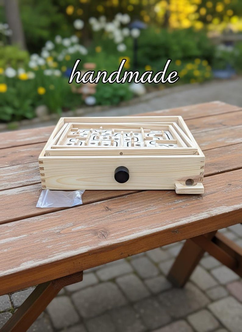 Puede incluir: Un juego de laberinto de madera hecho a mano con una perilla de control negra. El juego est&aacute; sobre una mesa de madera al aire libre, con la palabra "handmade" escrita en la parte superior. El juego presenta un dise&ntilde;o de laberinto.