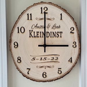 May include: A wooden clock with a natural wood grain finish. The clock face is white with black numbers and hands. The clock is personalized with the names "Austin & Leah KLEINDINST" and the date "5-15-22".
