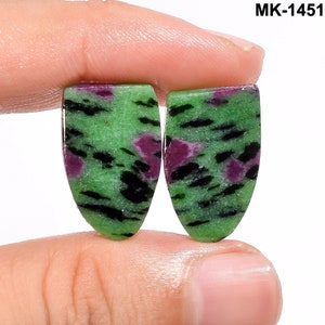 Op de afbeelding: Een paar ovale cabochon edelstenen in groen, zwart en roze. De stenen hebben een gevlekt patroon.