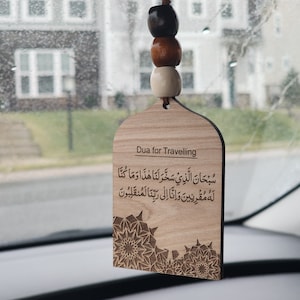 May include: A wooden car charm with an Islamic prayer for traveling in Arabic script. The charm is shaped like an arch and has a decorative floral pattern. The text reads "Subhana alladhi sakhkhara lana hadha wa ma kunna lahu muqrinin wa inna ila rabbina lamunqalibun".