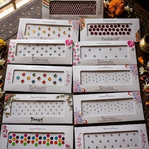 May include: A collection of Parineeta brand bindi stickers in various colors and designs. The boxes feature diamond and gem-like accents, with text including "Diamond Collection" and brand names like "Padmavati" and "Tanya."