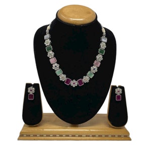 May include: A silver necklace with a row of square-shaped gemstones in shades of pink, green, and white. The necklace is paired with matching earrings with a single pink gemstone.