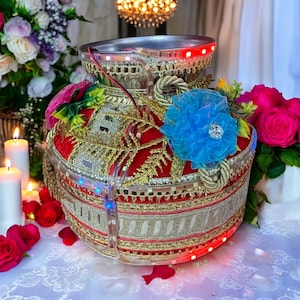 May include: A red and gold decorated pot with a blue flower and lights. The pot is decorated with gold trim and a rope-like design. The pot is lit up with red and blue lights.