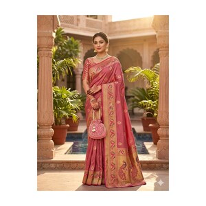 May include: A woman wearing a dusty rose saree with gold accents and a matching purse. The saree features intricate patterns and a peacock design on the border. The background includes architectural elements and potted plants.