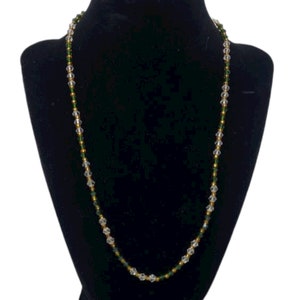 May include: A delicate necklace made with clear and green glass beads. The necklace is strung on a gold-colored thread.