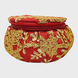 May include: A small, round red fabric pouch with a zipper closure. The pouch is adorned with intricate gold and white floral embroidery. The design is symmetrical, with the embroidery covering the entire surface of the pouch.