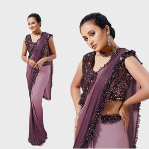 May include: A two-piece purple saree with a sequined top and a flowing skirt. The sleeveless top is heavily embellished with sequins, and the saree features ruffled edges. The color palette includes shades of purple and lavender, creating an elegant look.