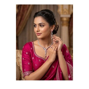 May include: A woman wearing a matching jewelry set, including a necklace, earrings, and rings. The jewelry features a silver-tone metal with clear and red gemstones. She is wearing a magenta-colored top and a matching sari.