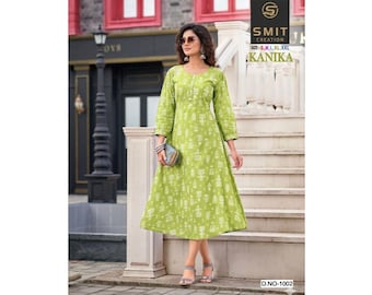 May include: A light green, knee-length dress with a white floral pattern. The dress has three-quarter sleeves and a scoop neckline. The image also shows a small clutch and sandals. The text "KANIKA" is visible on the upper right.