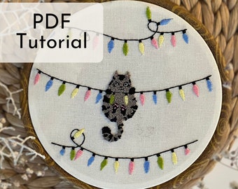 May include: A PDF tutorial for a cross-stitch embroidery project featuring a gray cat hanging from a string of colorful lights. The cat is stitched in a simple, cartoon style. The lights are a mix of pink, blue, green, and yellow.