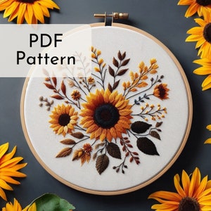 Könnte beinhalten: Ein PDF-Muster zum Sticken mit einem Strauß Sonnenblumen und Blättern in Gelb-, Orange-, Braun- und Grüntönen. Das Muster ist in einem hölzernen Stickrahmen dargestellt.