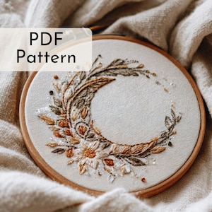 Könnte beinhalten: Gesticktes Hoop-Art mit floralem und Halbmond-Design. Die Stickerei weist Braun-, Beige- und Goldtöne auf, mit einem Holzreifen. Der Text "PDF Pattern" befindet sich in der oberen linken Ecke. Das Kunstwerk befindet sich auf einem cremefarbenen Stoff.