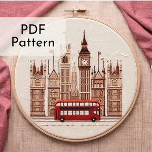 Può includere: Arte di ricamo a cerchio che presenta un autobus rosso a due piani che guida davanti a monumenti iconici di Londra, tra cui Big Ben e le Case del Parlamento. Il design è ricamato in una varietà di colori su un tessuto color crema.