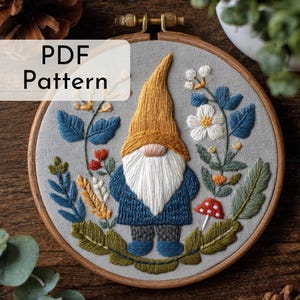 May include: Embroidered gnome design in a wooden hoop. The gnome wears a yellow hat, blue coat, and white beard, surrounded by floral and leaf details. The text "PDF Pattern" is displayed on the upper left.