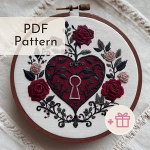 May include: An embroidery hoop featuring a heart-shaped design with a keyhole, surrounded by roses and foliage. The heart is a deep red color, with black vines and leaves. The text "PDF Pattern" is visible.