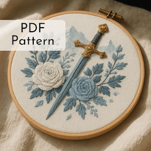 May include: Embroidered hoop art with a sword design. The embroidery includes a gold hilt, light blue blade, two roses, blue leaves, and the text "PDF Pattern". The artwork is set against a cream-colored fabric, within a wooden hoop.